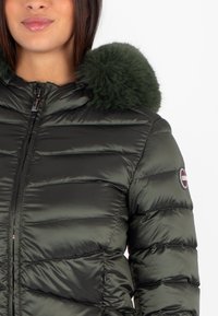 Giacca a vento verde con cappuccio rifinito in pelliccia sintetica, dotata di chiusura con zip e texture a quadri orizzontali. Patch con logo sulla manica.