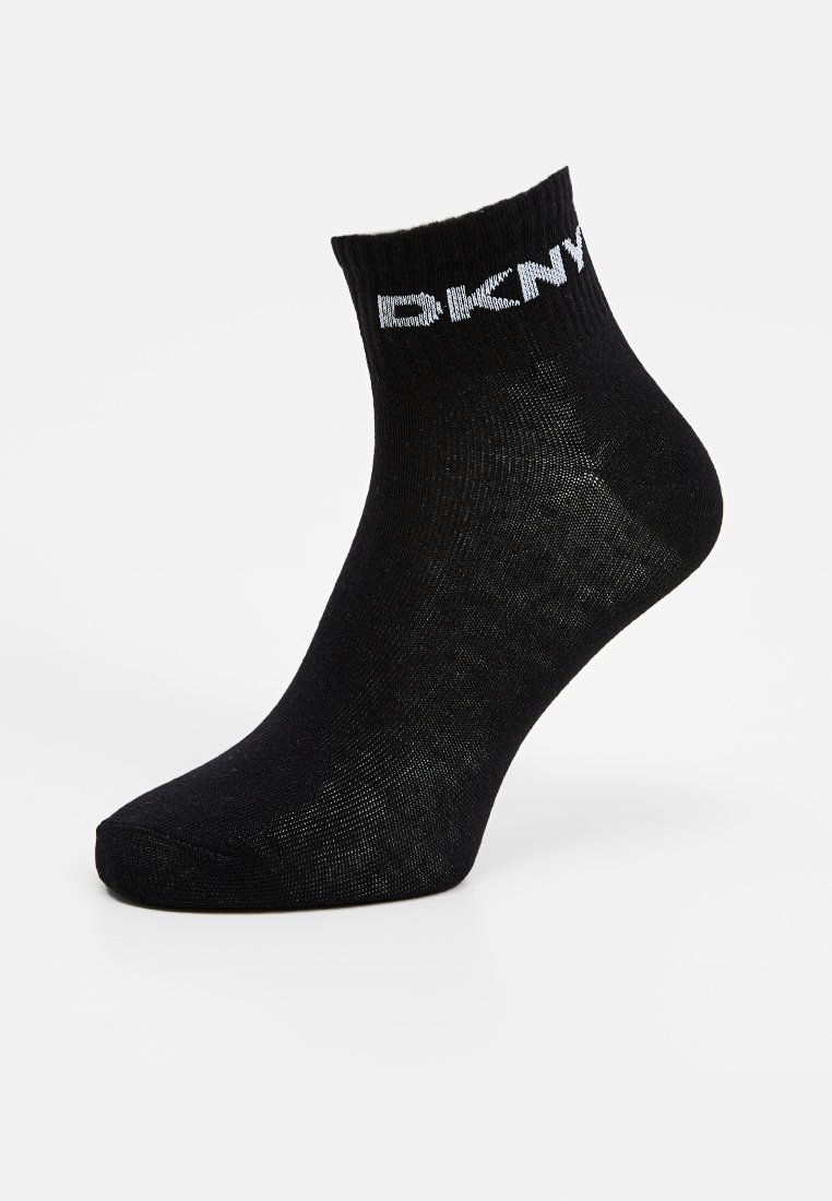 Schwarze Knöchelsocke mit gerippter Textur und einem weißen Logo am Bündchen. Das Material wirkt glatt und ist geeignet für Freizeitkleidung.