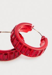 Käe paari läbipaistvaid punaseid rõngasehteid, millel on ristkülikukujulised faceted segmentid ja metallkinnitused valgel taustal.