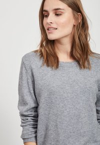 Pull en maille gris avec un col rond, des manches longues et des poignets côtelés. Texture douce avec un léger motif chiné.