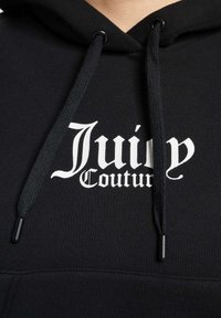 Černá mikina s kapucí vyrobená z bavlny, s přední kapsou. Logo "Juicy Couture" v bílé barvě, ve stylu gotického písma, na hrudi. Šňůrka na kapuci.