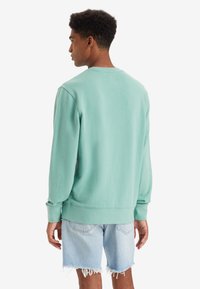 Mintgroene sweatshirt met een ronde hals, geribbelde mouwen en zoom. Gepaard met lichtblauwe denim shorts met rafelige randen.