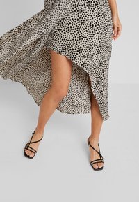 Epäsymmetrinen, kevyt, pilkullinen mekko korkealla halkiolla; yhdistetty mustiin hihnasaappaisiin ja sileään tekstuuriin.