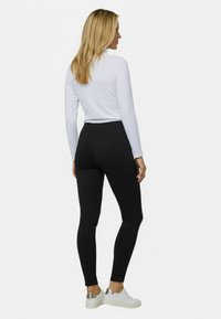 Leggings negros hechos de un tejido elástico, combinados con una camiseta ajustada de manga larga blanca. El modelo lleva zapatillas blancas con detalles plateados.