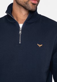 Felpa zip-up blu navy realizzata in morbido tessuto, con colletto alto e zip argentata. Logo dorato ricamato sul petto.