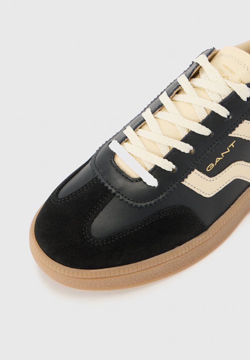 Baskets noires et crème avec un mélange de cuir et de daim, dotées de lacets crème, d'une semelle en gomme texturée et d'un détail logo discret.