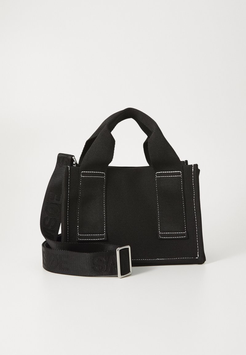 Czarna torba na ramię z dwoma uchwytami u góry, regulowanym paskiem, srebrnym okuciem i białymi przeszyciami wzdłuż krawędzi. Kompaktowy prostokątny kształt.