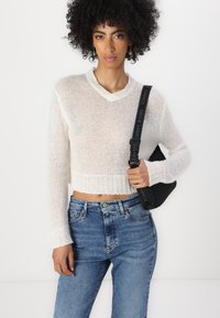 Suéter blanco, de punto, recortado y con escote en V, que presenta mangas largas. Combinado con unos pantalones vaqueros de tiro alto en azul y un bolso negro con correa de logo.
