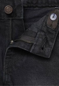 Crni denimski materijal s vidljivim zatvaračem i kopčanjem na dugme, sa detaljima šivanja i teksturiranom površinom.