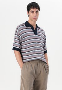 Gestricktes Polo-Shirt mit kurzen Ärmeln in Streifenmuster aus Pink, Blau und Marineblau. Mit tiefem V-Ausschnitt und festem Marineblauen Kragen. Weiches, strukturiertes Material.