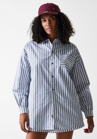 Striped button-up shirt in blue and white. Features a pocket with a logo, long sleeves, and a relaxed fit. Cotton fabric with a smooth texture.