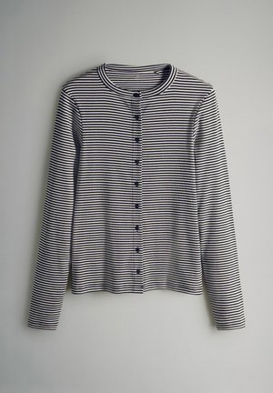 Hosszú ujjú, gombolós kardigán tengerészkék és krémszínű csíkokkal. Kerek nyakkivágással és hét, elöl végig futó, az anyaghoz illő gombbal rendelkezik. Puha anyagból készült.