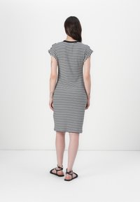 Svart og hvit stripete kjole, tettsittende design, korte ermer, midt på leggen lengde, laget av mykt stoff. Brukt med svarte sandaler.