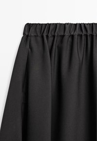 Gonna nera in tessuto con vita elasticizzata, presenta una sottile texture e delicate pieghe che enfatizzano il suo movimento e caduta.