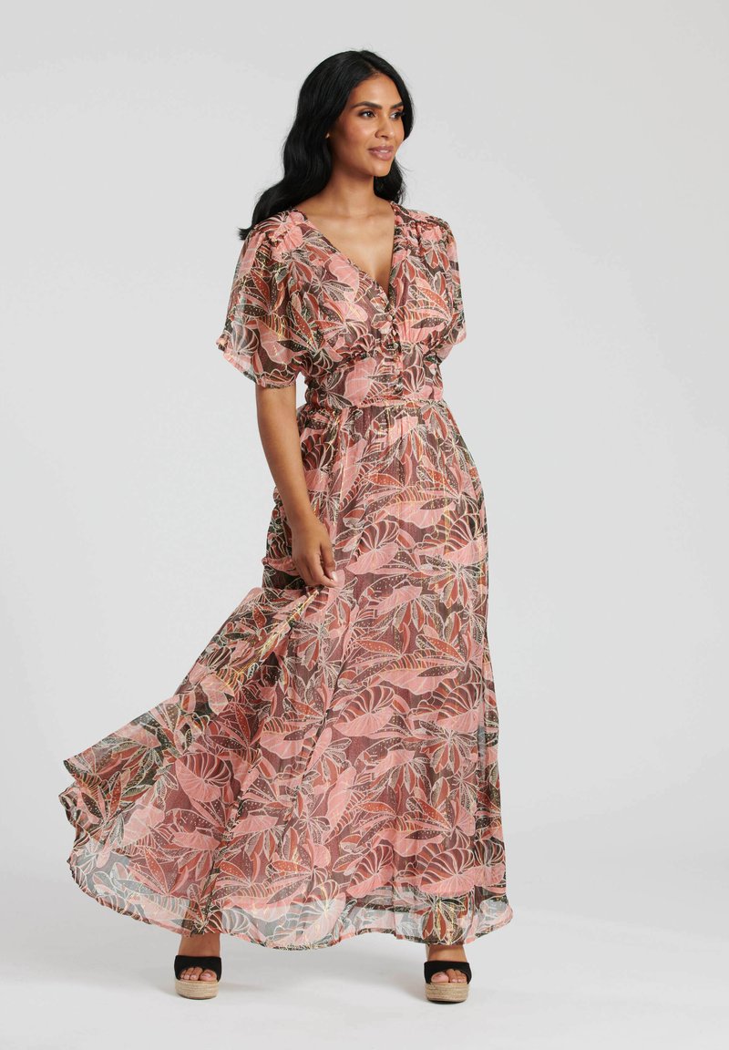 Abito maxi in tessuto trasparente con un motivo di foglie rosa e verdi. Presenta maniche corte e svolazzanti e una vita increspata. Indossato con sandali con piattaforma neri.