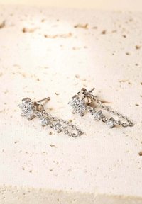 Silberne Ohrhänger mit floralen Motiven und mehreren klaren Kristallen. Die Ohrringe haben ein hängendes Kettendesign und eine polierte Metall-Oberfläche.