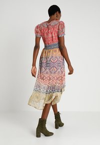 Robe midi colorée avec manches bouffantes, taille élastique et jupe à motifs présentant des nuances de rouge, jaune et violet. Bottines vert olive.