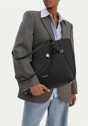 Osoba nosící šedý sako s proužky a světle modrou košili, držící velkou černou kabelku Gino Rossi s ramenními popruhy.