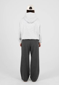 Šedá mikina s kapucí, kombinovaná s volně střiženými tmavě šedými kalhotami. Na hlavě je světlá kšiltovka nasazená dozadu. Jednoduchý, neformální design.