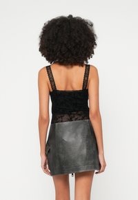 Camisola de renda preta com alças ajustáveis, combinada com uma minissaia de couro cinzento com bolso lateral e textura suave e fosca.