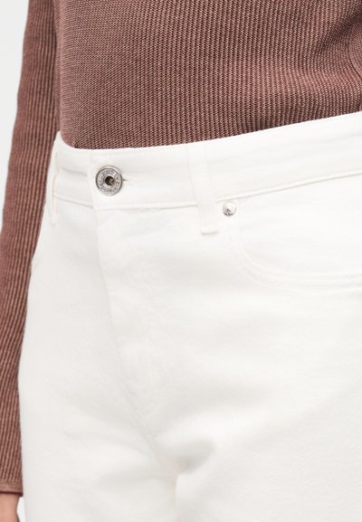 Κοντινό πλάνο της μέσης με άσπρο τζιν παντελόνι με ασημένιο κουμπί και καφέ μακρυμάνικη μπλούζα με υφή.