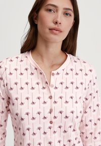 Roze langemouw top met een bloemenpatroon in donkerrood, een ronde halslijn met een drie-knopen placket, en een zachte, gladde textuur.