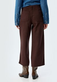Brune brede bukser lavet af slidstærkt stof, med baglommer og en ren kant. Kombineret med cowboystøvler og en denimtop.