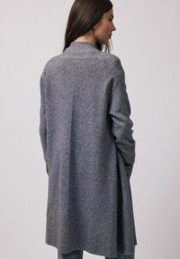 Cardigan long à devant ouvert en tissu gris doux. Il présente un col simple et une coupe décontractée, avec des épaules tombantes et un motif en tricot texturé.