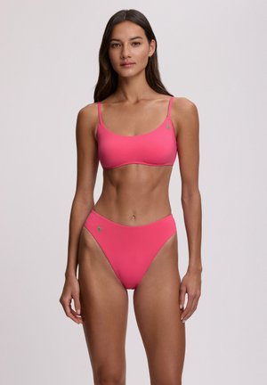 Bikini rosa acceso con scollo a U e spalline sottili. Slip a vita alta con piccolo dettaglio logo verde su entrambi i pezzi. Tessuto liscio.