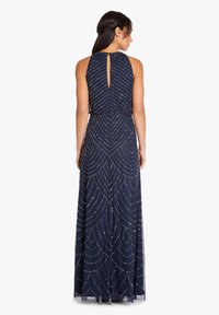 Robe de soirée bleu marine avec un col haut et un dos en forme de trou de serrure, ornée de perles argentées complexes dans des motifs géométriques sur un tissu fluide.