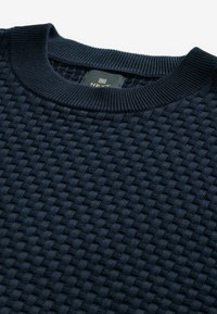 Marineblauer gestrickter Pullover mit einem strukturierten, gewebten Muster. Der gerippte Halsausschnitt sorgt für Stabilität. Das Etikett zeigt die Marke "NEXT".