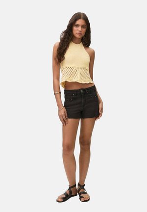 Geel gebreide haltertop met een golvende zoom, gecombineerd met zwarte denim shorts en zwarte sandalen met bandjes.