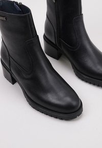 Botas de tobillo de cuero negro con un acabado suave, puntera redondeada y tacón cuadrado. Presentan paneles elásticos laterales y una cremallera para facilitar el uso.