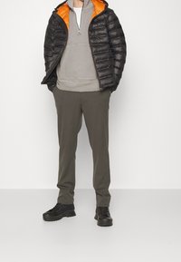 Giacca a vento nera con fodera arancione, felpa grigia con zip a metà, pantaloni grigi e scarpe nere. Design semplice con tessuto testurizzato.
