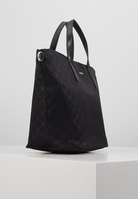 Schwarze Tragetasche mit strukturiertem Muster, glatten Ledergriffen, rechteckiger Form und silbernen Hardware-Akzenten. Besitzt ein dezentes Logodetail.