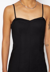 Robe noire ajustée avec des bretelles spaghetti, un décolleté droit et des détails de couture. Présente un éclat subtil et une texture de tissu lisse.