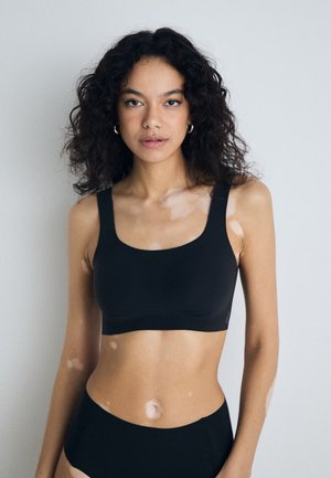 Zwarte naadloze bralette met brede bandjes en een vierkante halslijn. Gladde textuur, minimalistisch ontwerp en geen zichtbare sluitingen.