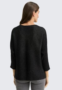 Pull noir à manches longues avec une texture côtelée et un léger éclat. Présente une coupe ample et décontractée avec un col rond, vu de l'arrière.