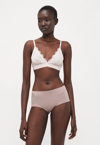 Lace bralette in cream with a scalloped edge and adjustable straps, paired with seamless nude boyshorts, featuring a smooth texture.