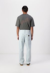 Light blue, loose-fitting jeans with back pockets and a label, paired with a dark gray t-shirt featuring red lettering on the back.