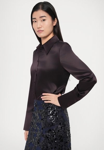 Tume lilla satiinist pluus terava kraega ja pikkade varrukatega, millele on kombineeritud seemnetega kaunistatud tumesinine seelik keerukate lillemustritega.