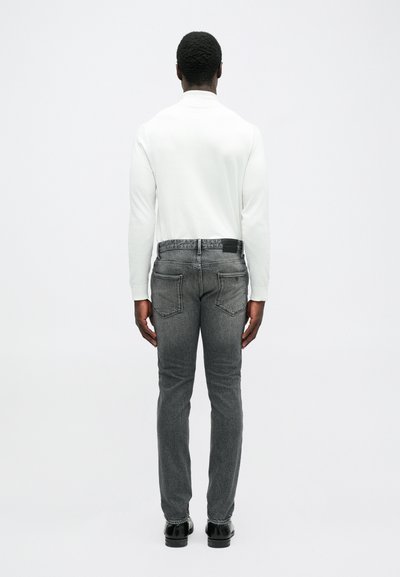 Λευκό πουκάμισο με μακριά μανίκια σε συνδυασμό με μαύρα τζιν, παρουσιάζοντας εφαρμογή slim fit, κλασικό σχέδιο πέντε τσέπες και ομαλή υφή.