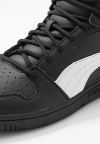 Black high-top sneaker with black laces, perforated toe, white side stripe, and textured sole on white background.