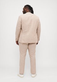 Conjunto de traje beige claro hecho de tela texturizada, que incluye una chaqueta de un solo botón y pantalones ajustados, combinados con zapatillas blancas.