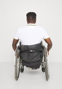Bílá polo košile s černými a žlutými detaily, kterou nosí osoba na invalidním vozíku, sedící z pohledu zezadu, viditelná černá tkanina vozíku.