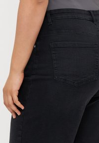 Vaqueros de mezclilla negros de cintura alta, con un único bolsillo trasero y una textura suave. El diseño enfatiza una silueta ajustada.
