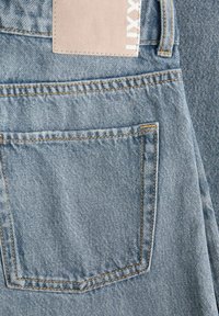 Ανοιχτό μπλε τζιν με ορατή πίσω τσέπη, θηλιά για ζώνη και μπεζ ορθογώνια ετικέτα ραμμένη πάνω από την τσέπη.