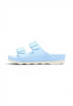 Sandalia azul claro tipo slip-on con dos correas ajustables con hebilla y una suela blanca texturizada, diseñada para uso casual.