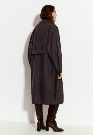 Dolga rjava volnena plašča z ozkim pasom, ovratnikom in padlimi rameni, v kombinaciji z rjavimi usnjenimi škornji do kolen.