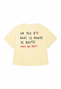 Yellow oversized t-shirt with black and red text on the back: "Un peu d'♥ dans ce monde de brutes (mais pas trop)."